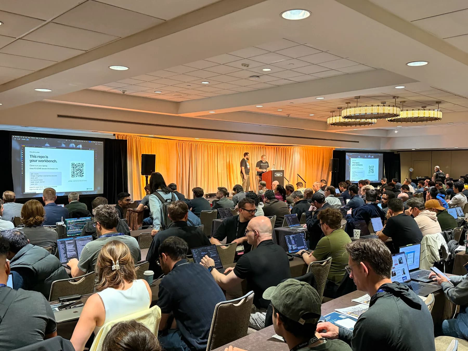A full workshop room at AI Engineer New York, with attendees working at tables and the presenters on stage.