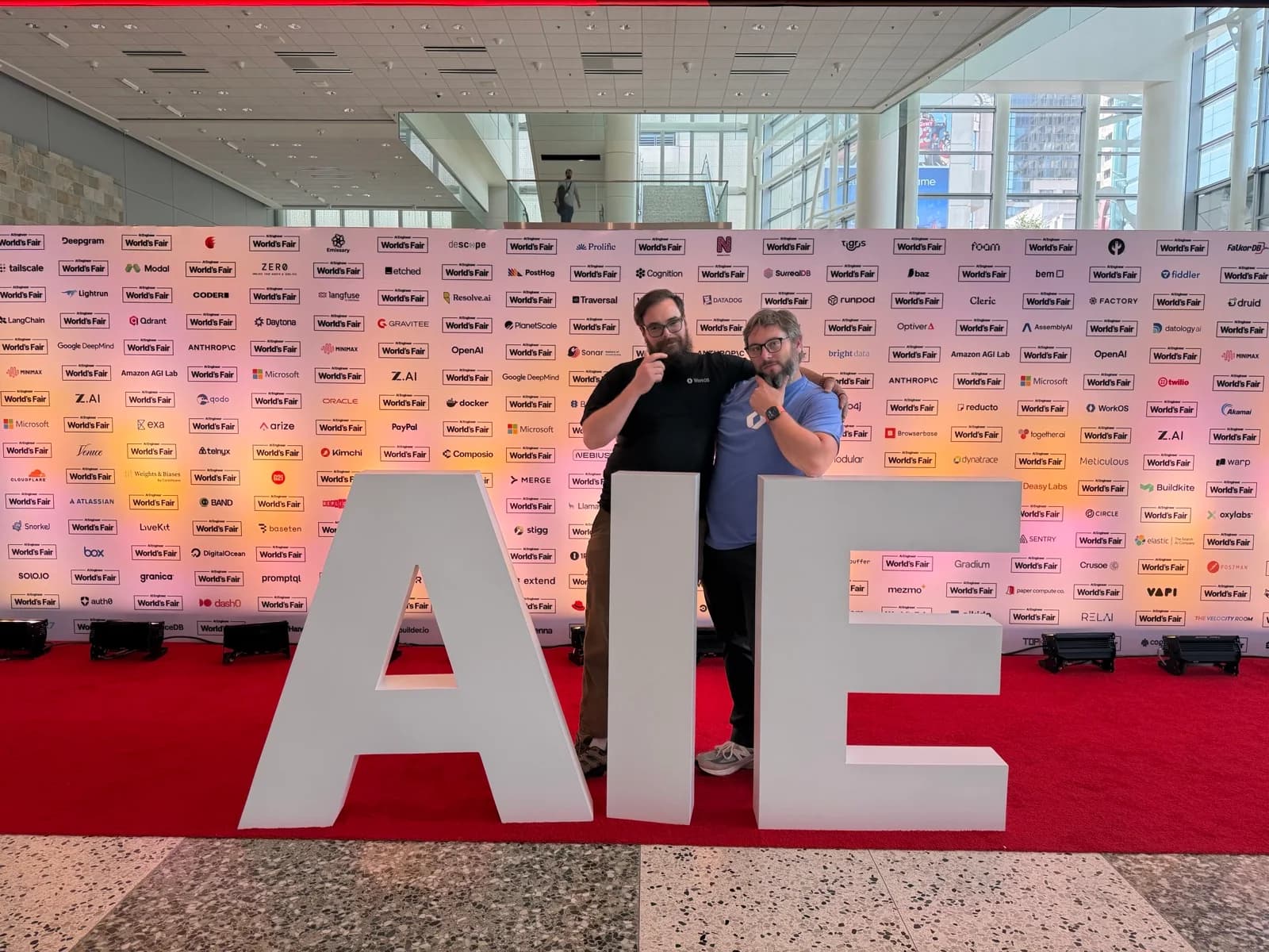 Zack and Nick standing behind the large AIE letters in front of the conference sponsor wall.